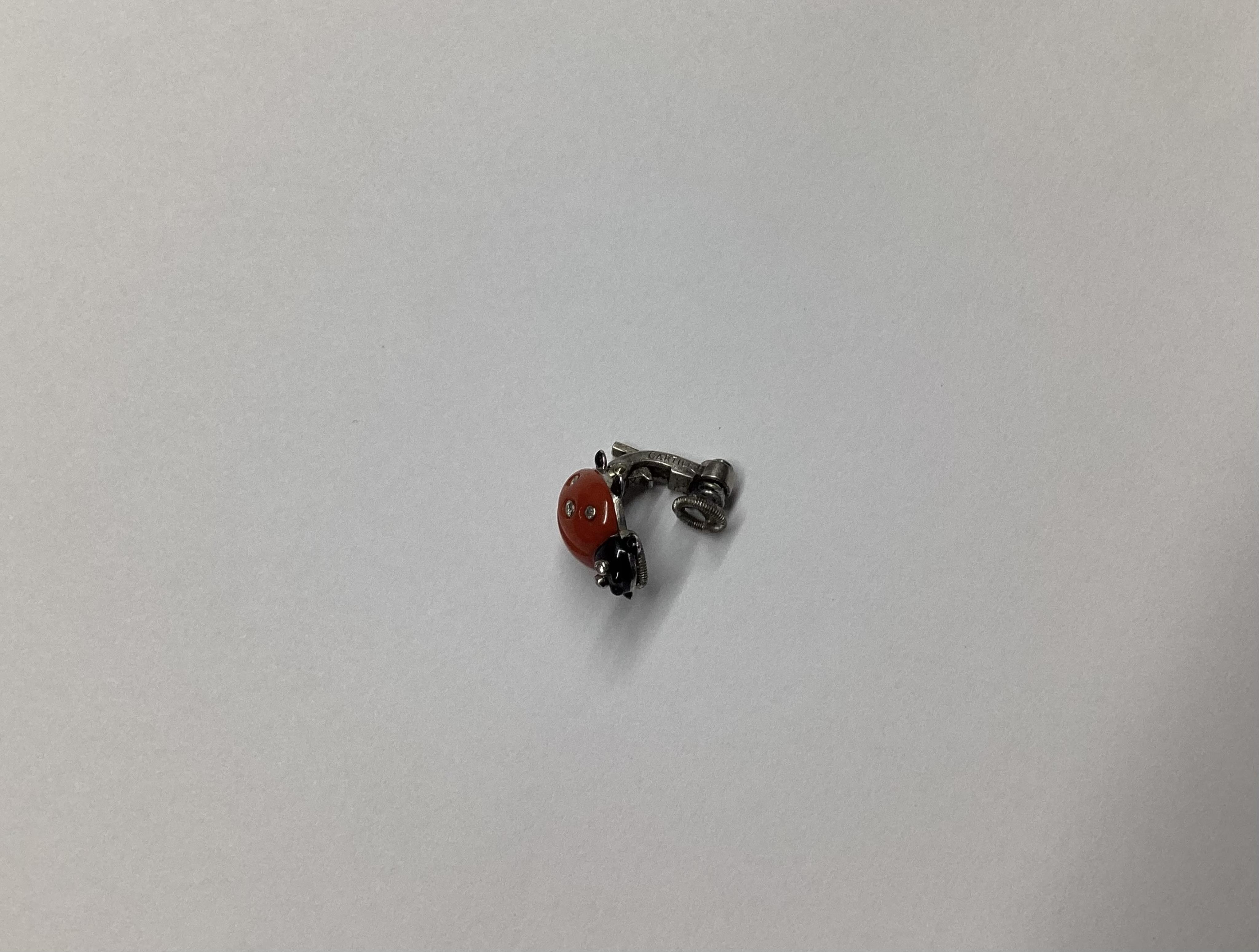 A pair of white metal, enamel, coral and diamond ladybird ear clips, bearing Cartier, New York signature and inscribed 18k